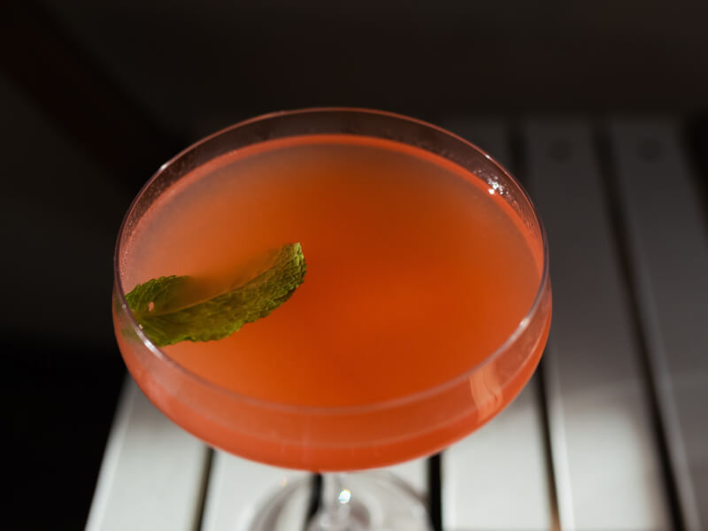 Red cocktail garnished with a leaf. 